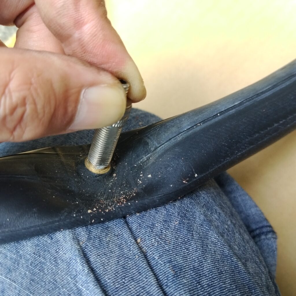 自転車のバルブ根元のパンクの穴の周りを紙やすりの粉が入らないように押さえながら、紙やすりで荒らしていく